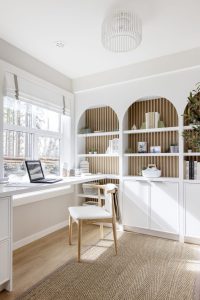 A wide-angle view of a modern desk in Surrey's The Loop townhome 'Cortland', showing a large window, overhead lighting, and light wood cabinetry.